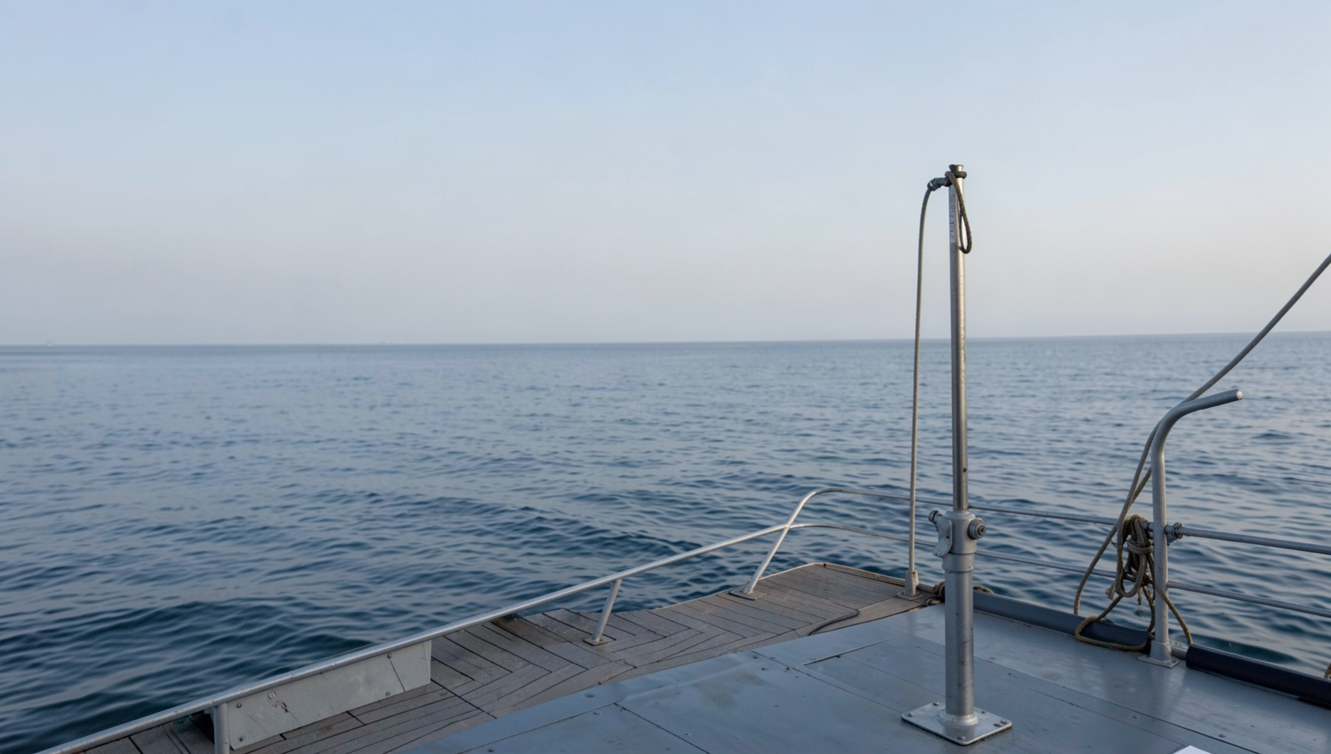 A deep drop rod in its holder on an open offshore deck at dawn, with calm water and soft sky beyond