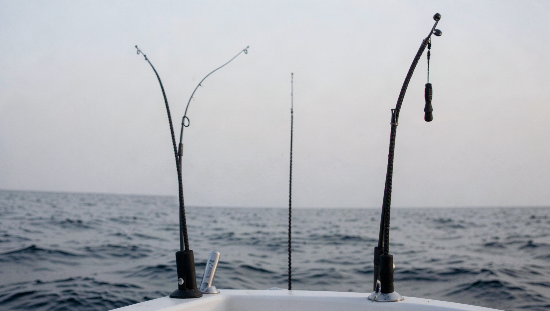 Deep-drop rods set in holders along an offshore boat's gunwale, heavy braid running straight down into dark water