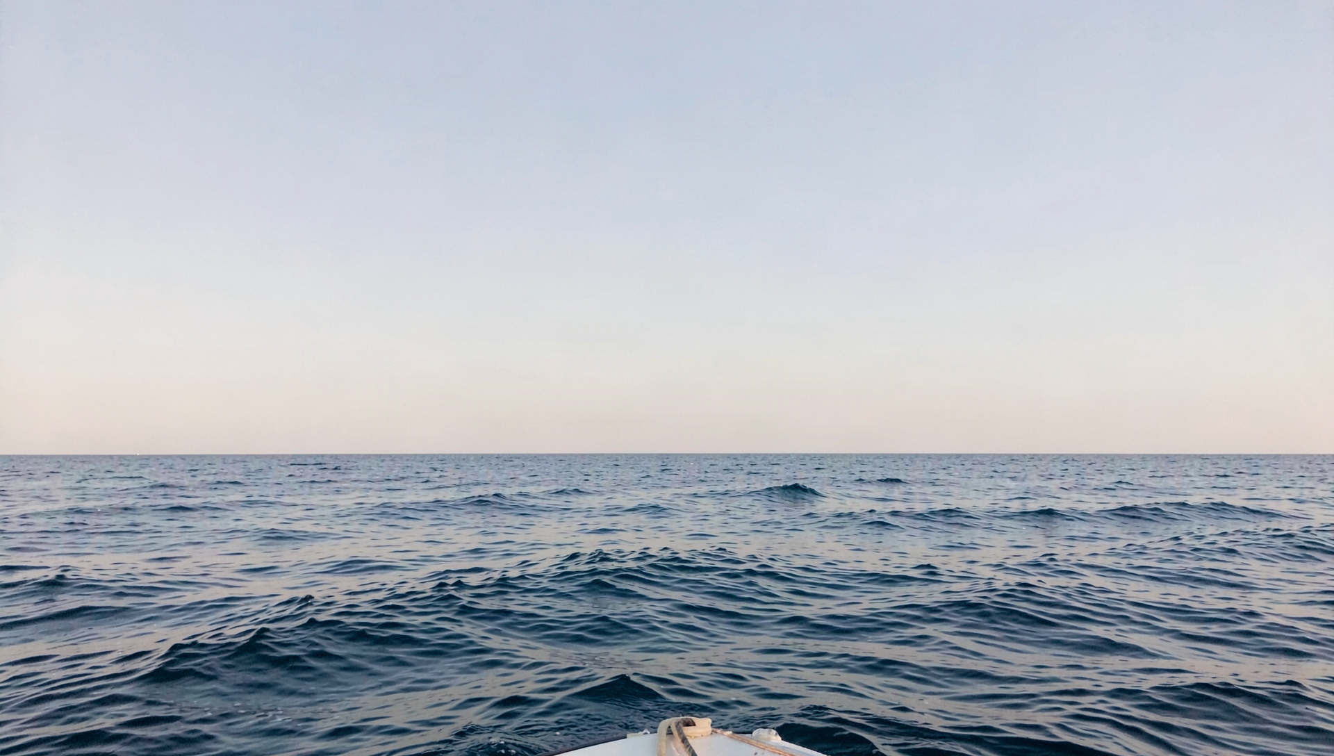 Wide photograph of open ocean at first light, calm water meeting an empty sky